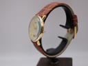 Side view of the Tissot T890K watch on a stand, showing the curved gold plated case and profile of the mineral glass.