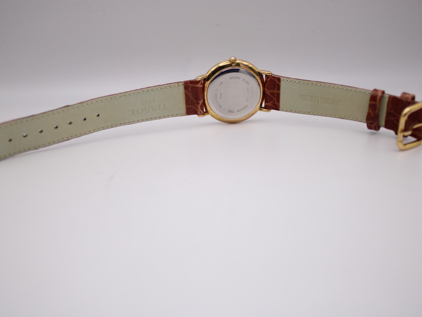 Underside view of the Tissot T890K watch laid flat, showing the "Genuine Leather" and "Tissot 1853" stamp on the strap lining.
