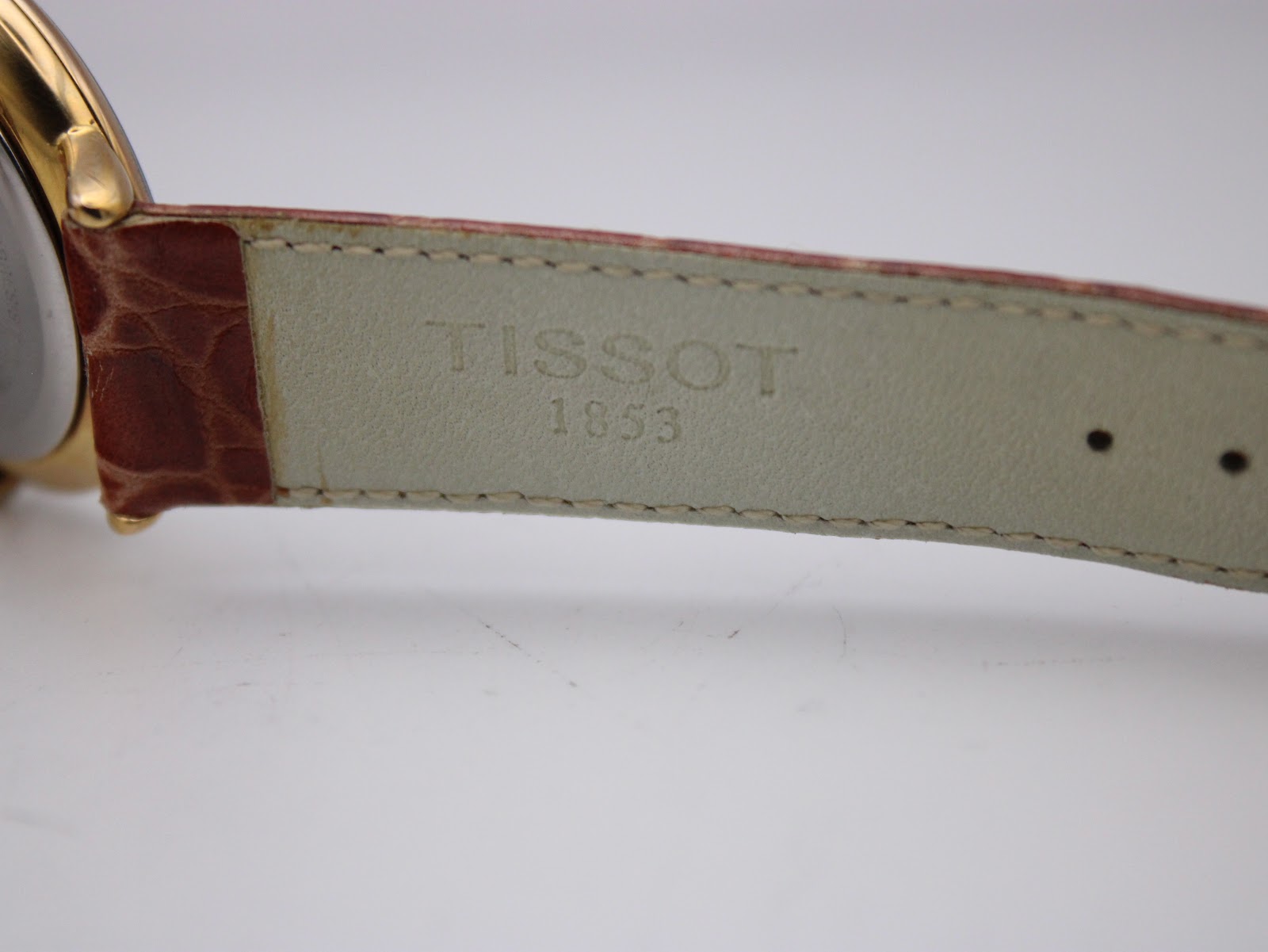 Close-up of the interior of the brown leather strap, showing the embossed "TISSOT 1853" branding near the lugs.