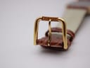 Close-up of the gold-tone buckle of the Tissot T890K, clearly showing the "TISSOT" signature engraved on the top bar.