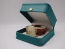 Tissot T890K watch presented open in a teal-coloured watch box with a gold crown emblem on the lid.