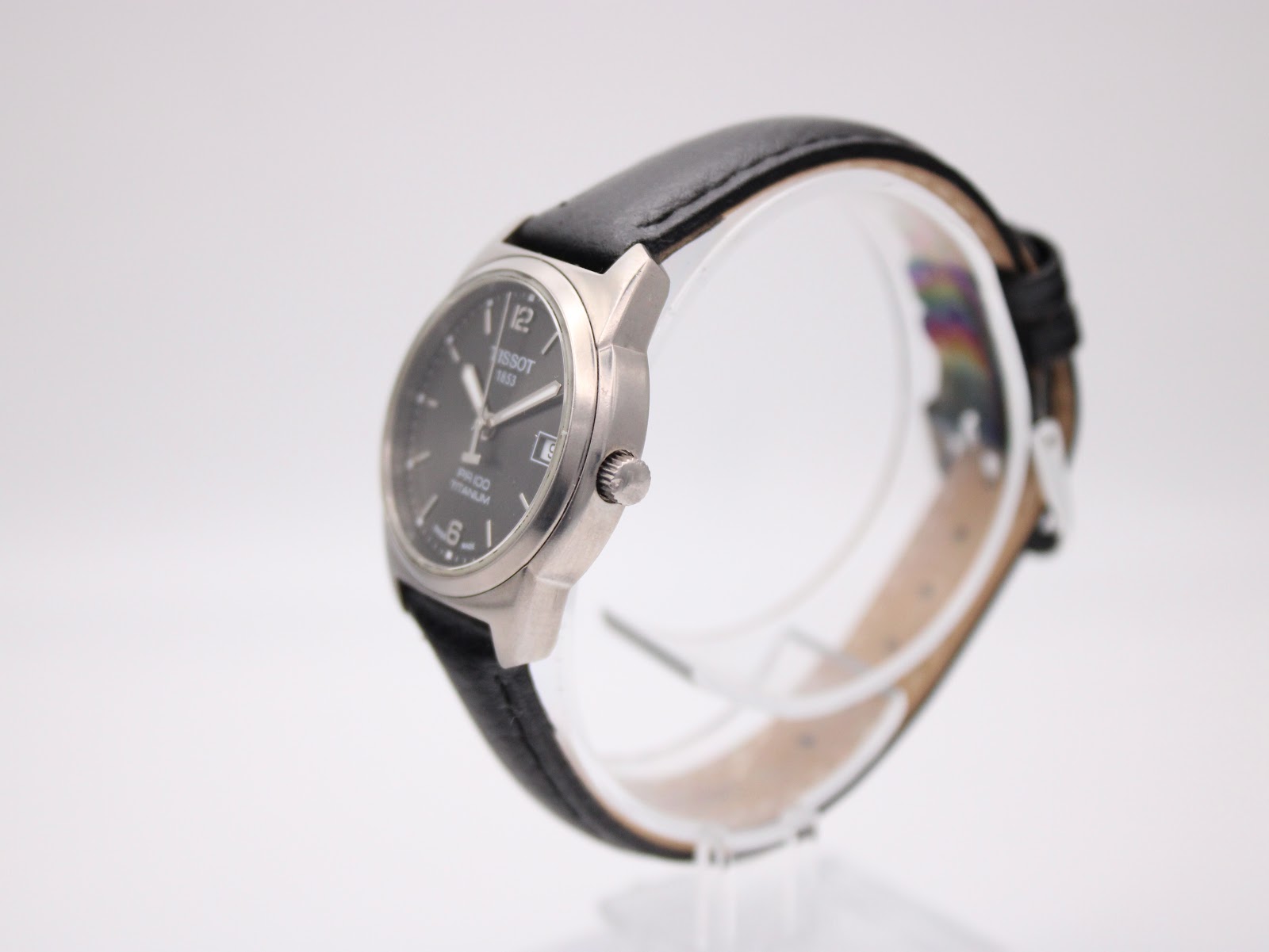 Right side profile of the Tissot watch showing the crown and brushed titanium case on a display stand.
