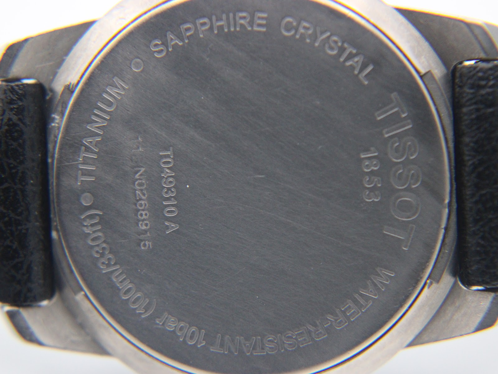 Close-up of the brushed titanium case back, showing model T049310A, serial number NQ268915, 'titanium', 'sapphire crystal', and 'water-resistant 10bar'.