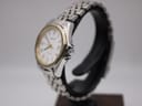 Angled side view of the Tissot watch from the right, highlighting the crown and polished case profile, with the two-tone bracelet curving around a display stand.