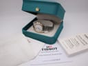 Overhead view of the watch sitting in its original teal Tissot box, surrounded by its user's manual, international guarantee card, and a dated service/purchase receipt.