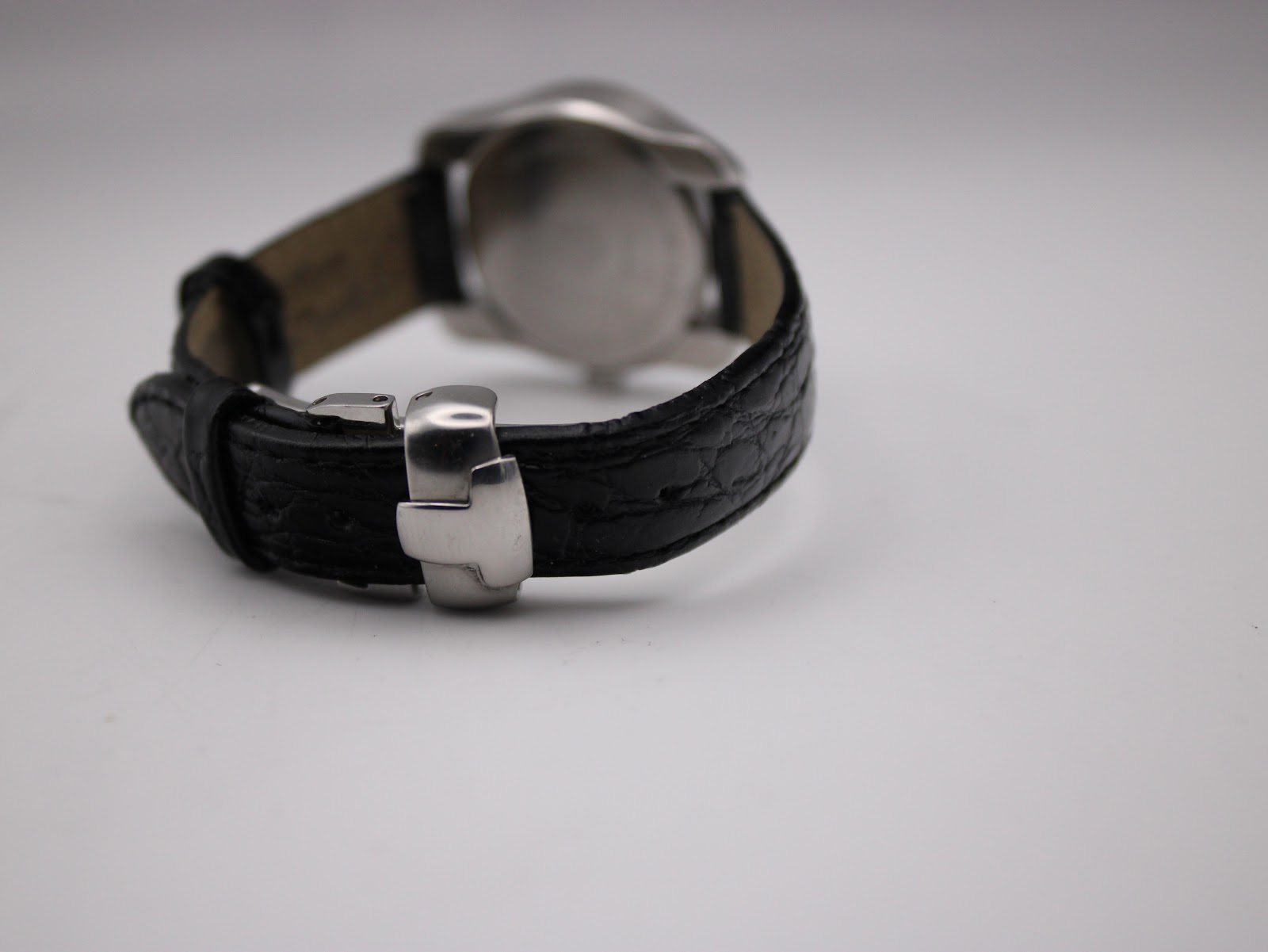 Side view of the Tissot watch, focusing on the closed butterfly deployment clasp on the black crocodile-grain leather strap.