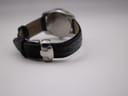 Side view of the Tissot watch, focusing on the closed butterfly deployment clasp on the black crocodile-grain leather strap.