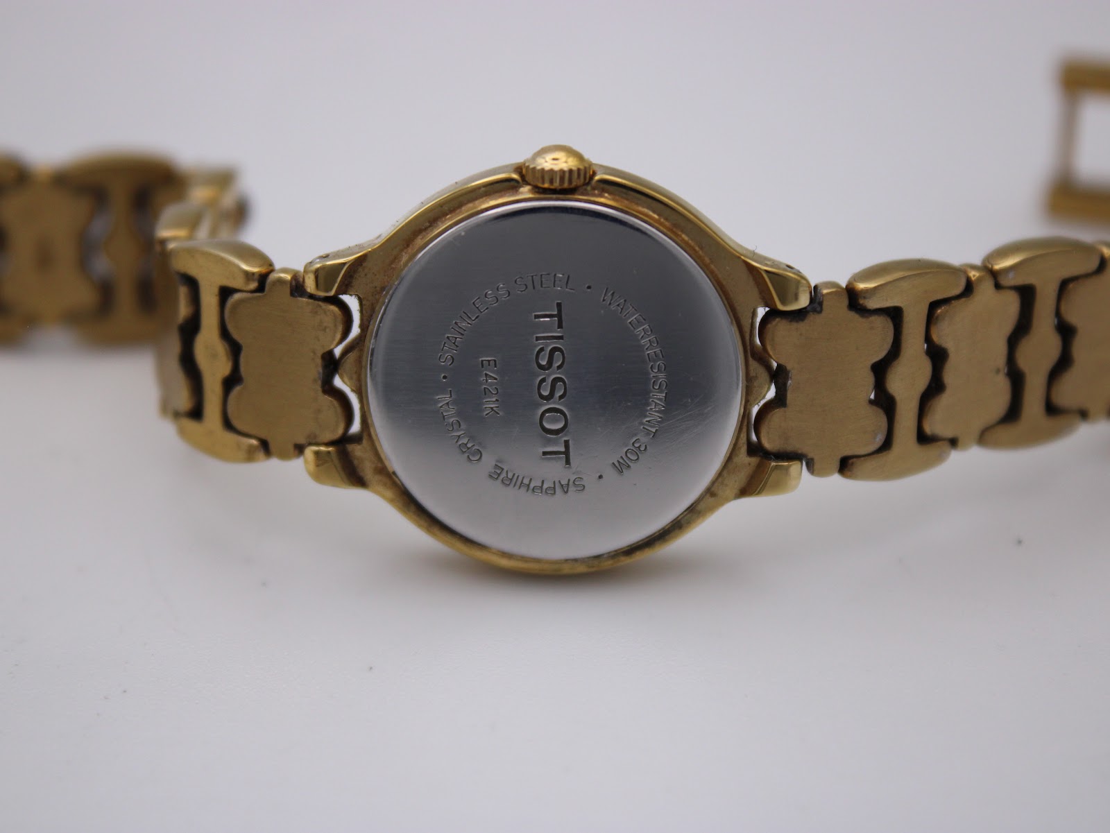 Close-up view of the stainless steel case back of the Tissot watch, clearly showing model number E421K, "stainless steel", "water resistant 30m", and "sapphire crystal" engravings.