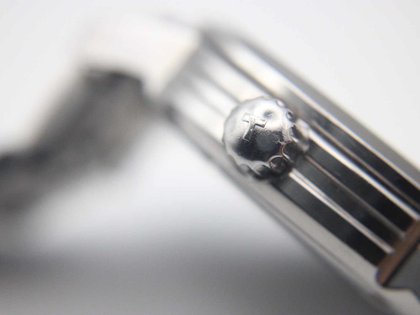 Macro close-up of the Tissot watch crown, showing the 'T' logo engraving.