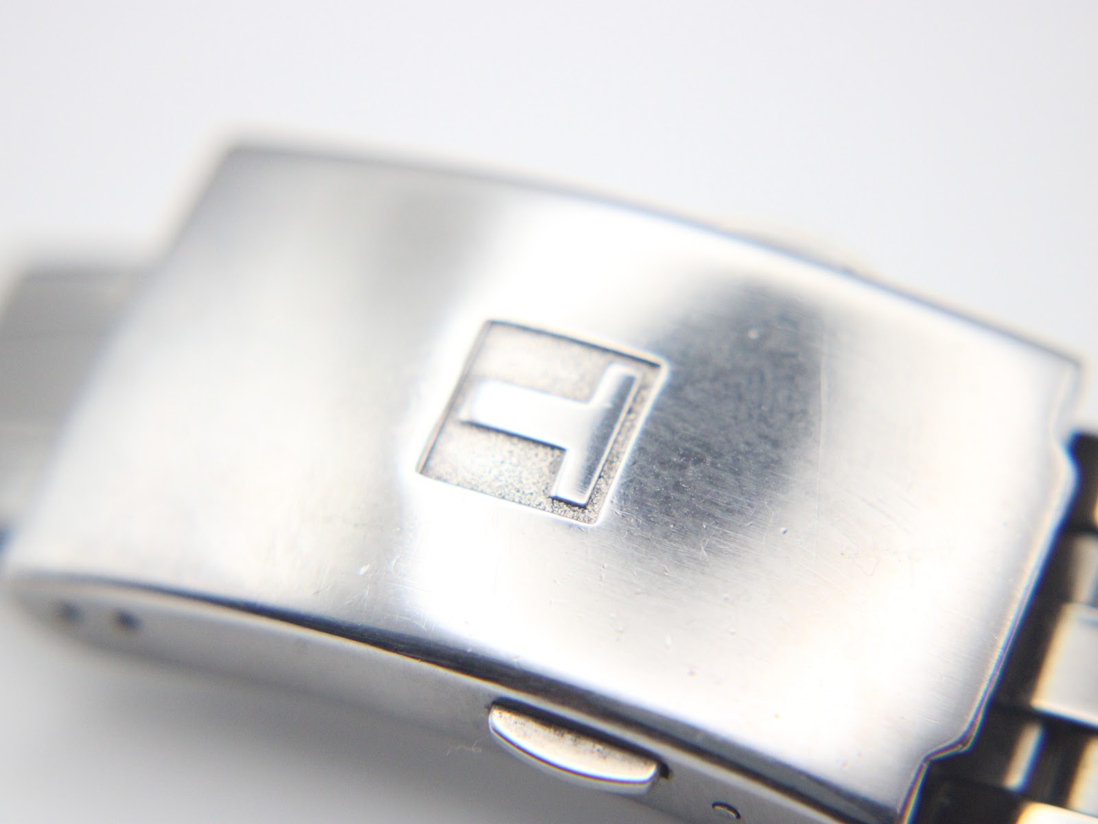 Close-up of the Tissot stainless steel bracelet clasp, clearly showing the embossed 'T' logo.