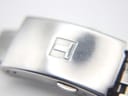 Close-up of the Tissot stainless steel bracelet clasp, clearly showing the embossed 'T' logo.