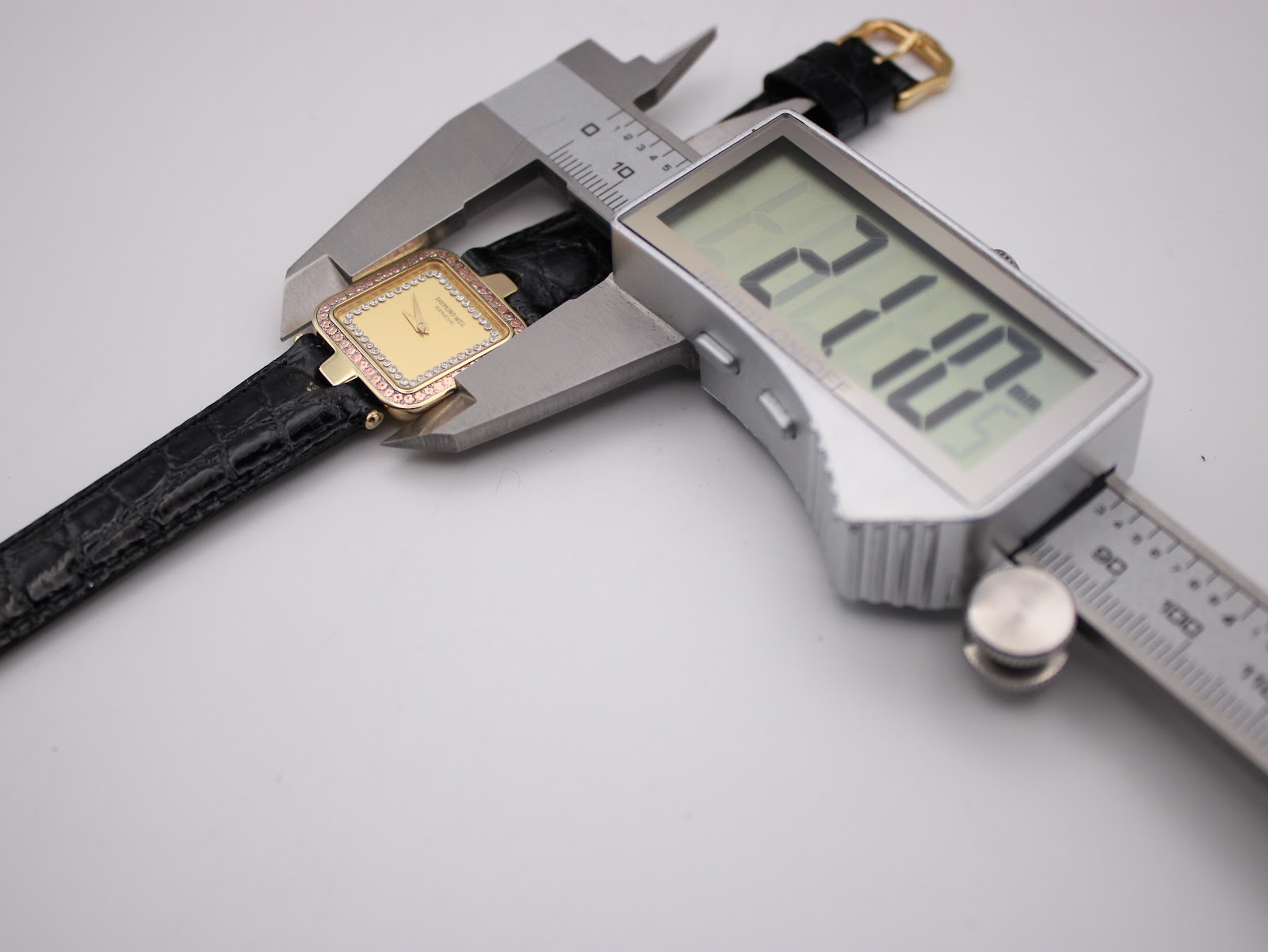 Top-down view of the watch being measured by a digital caliper, displaying a case width of 21.10mm.