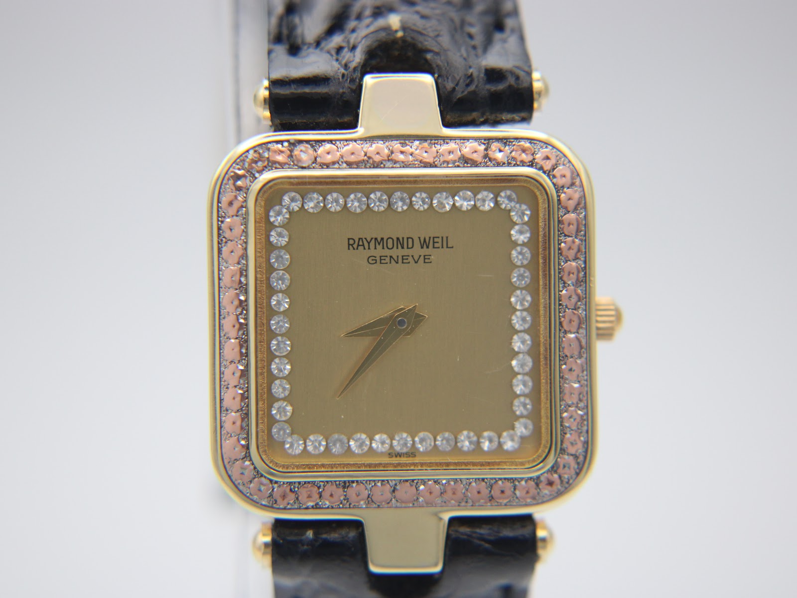 Close-up, straight-on view of the Raymond Weil champagne dial, 'RAYMOND WEIL GENEVE' text, central hour/minute hands, and double row of crystals.