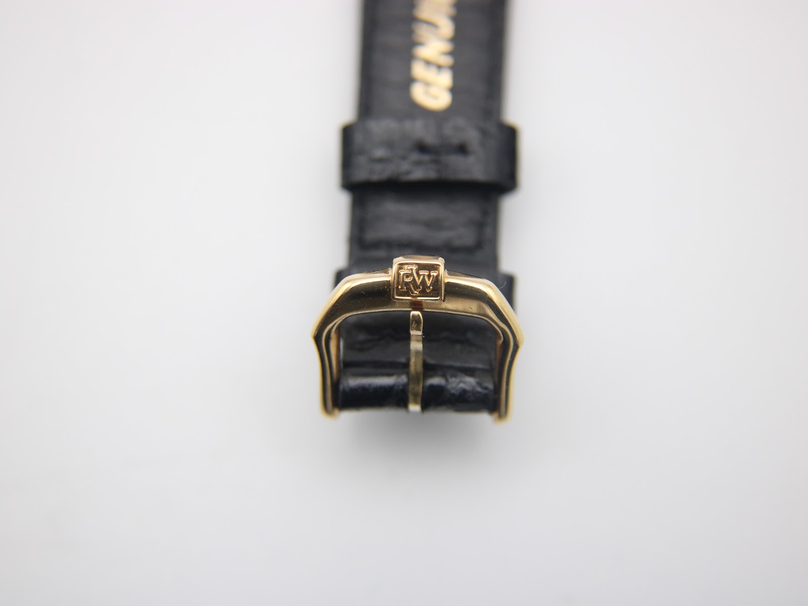 Close-up of the gold-tone buckle on the black leather strap, showing the engraved 'RW' logo.