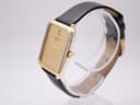 Angled side view of the Raymond Weil 713 watch on a transparent stand, showcasing the gold case and crown.