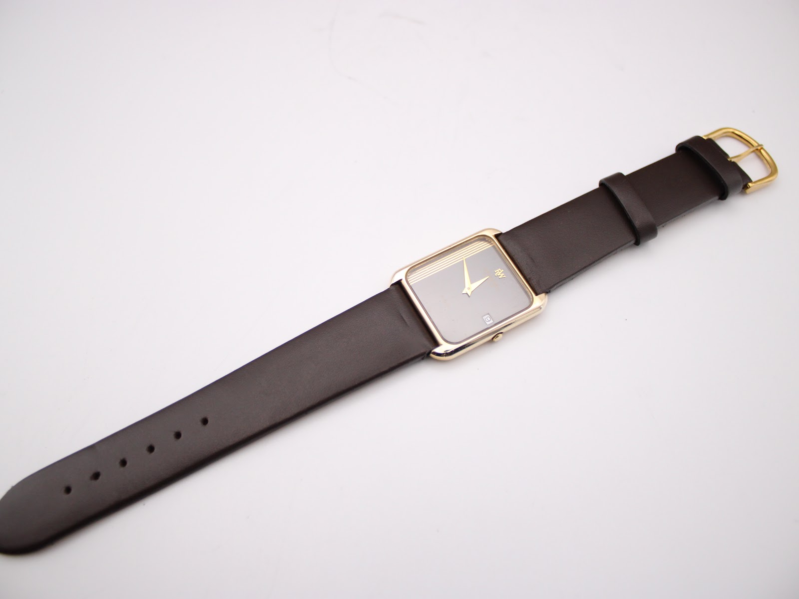 Full length view of the Raymond Weil 9118 with its dark brown leather strap and gold-tone buckle extended, against a white background.
