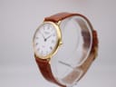 Angled side view of the Raymond Weil 5514 watch showing its gold case, coin-edge bezel, and brown strap on a display.